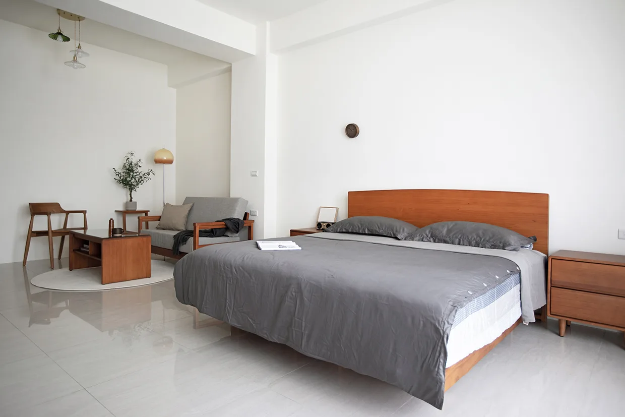 虎尾寮案臥室擺放Læsø萊斯漂浮床架，搭配藍灰色床包及枕頭，側邊擺放Sweet小八床頭櫃，臥室左側設計沙發休息區。